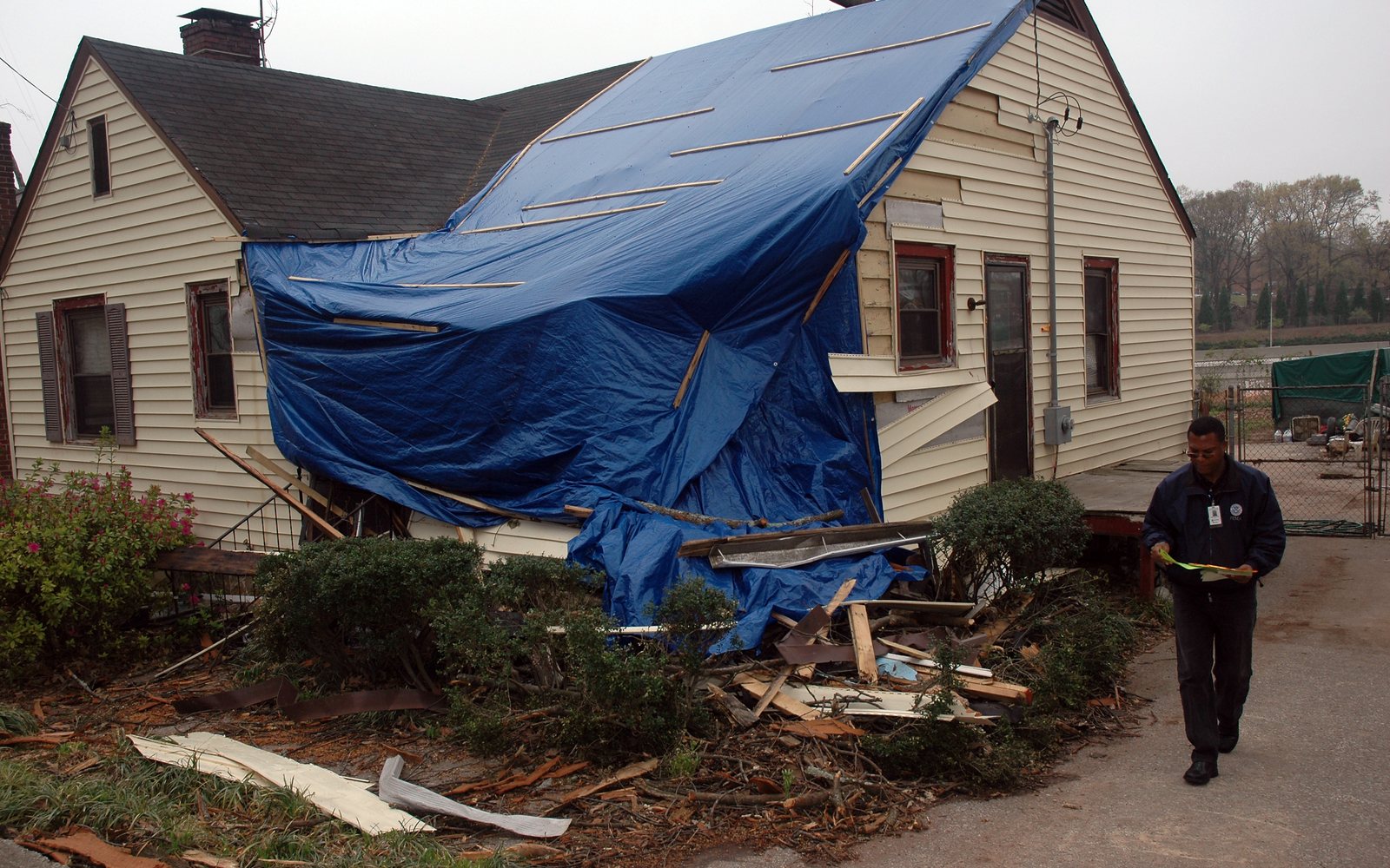 Collapsed house with a blue tarp and an inspector on the file